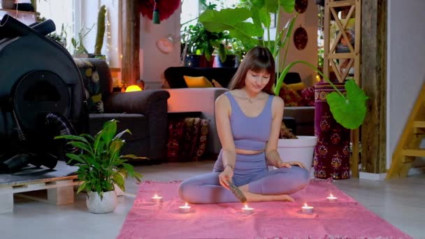 Woman sitting on floor, sets fire white sage incense for yoga meditation. — Stock video