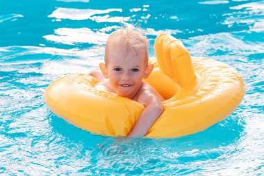 Güneşli bir günde yüzme havuzunda şişme şamandırayla yüzen küçük çocuk..