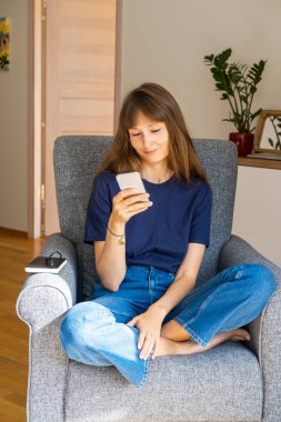 Cep telefonu kullanan ve koltukta oturan genç bir kadın..