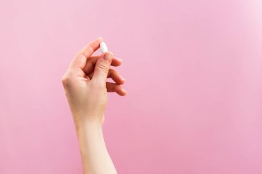 Pembe arka planda beyaz bir hap tutan kadın..