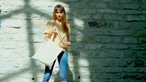 Woman in beige t-shirt holding white canvas tote bag. — Stock Video