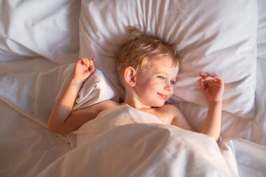 Tatlı çocuk uyandı ve yatağında güneşleniyor..