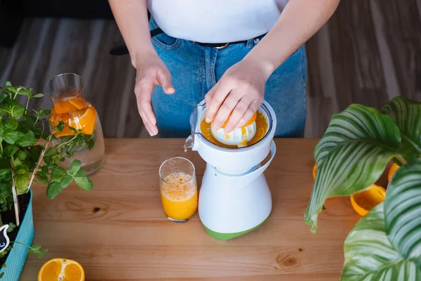 Bitkilerle dolu bir mutfakta taze portakal suyu yapan bir kadın..