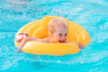 Güneşli bir günde yüzme havuzunda şişme şamandırayla yüzen küçük çocuk..