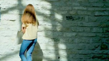 Bej tişörtlü bir kadın elinde beyaz bir çanta tutuyor. Kadın dönüyor ve gülümsüyor. Güzel ışık ve gölge oyunu. Yaşam tarzı kavramı.