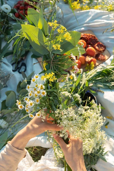 Unrecognized woman weaves a wreath of wild flowers for the summer solstice at master class. Vertical life style photo.