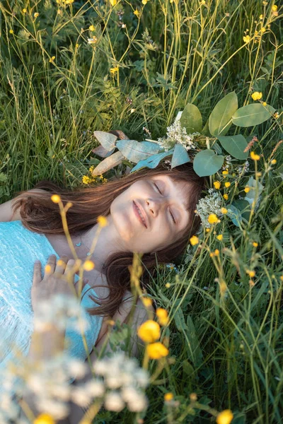 Woman with a flower wreath on her head lies in a field, enjoys the summer. Summer solstice day. Midsummer festival. Vertical photo.