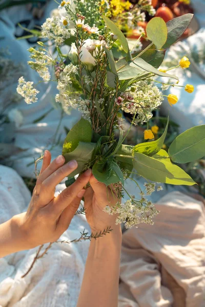 Unrecognized woman weaves a wreath of wild flowers for the summer solstice at master class. Vertical life style photo.