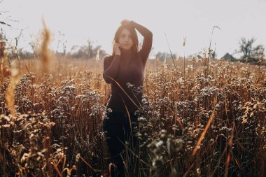 Kız kuru çimlerde sonbahar tarlasında günlük kıyafetlerle, tarafsız renklerle duruyor.
