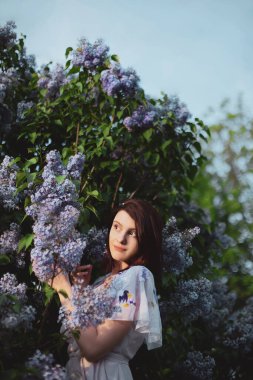 Romantik kızıl saç Bob tarzı kadın leylak rengi bahar çalılarının yanında duruyor.