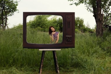 Kadın bahçedeki çimenlerde oturuyor eski moda televizyon çerçevesi, modern teknoloji ve akıl sağlığı