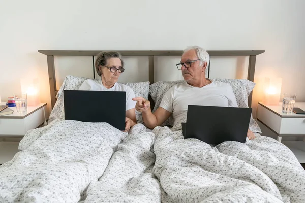 Yaşlanan yaşlı evli çift, erkek ve kadın. Evde, evde dizüstü bilgisayarlı ev işlerini kullanarak birlikte dinleniyorlar.