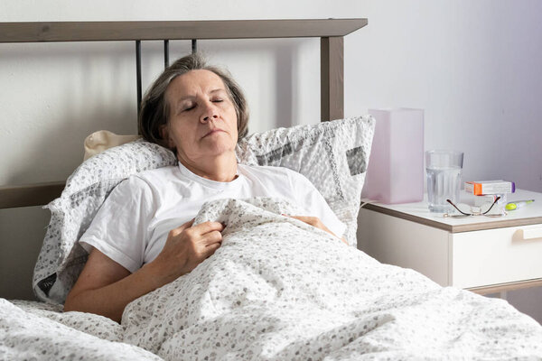 aging senior woman female in bed at home flat, tired sick ill alone retired and resting virus taking care unhappy sad.