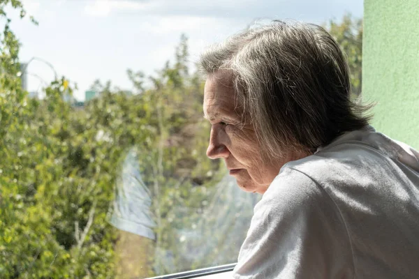 Üzgün yaşlı kadın yalnız başına evde kalır. Depresyonda olan koronavirüs izolasyonu. Dul, mutsuz, terk edilmiş pencere.
