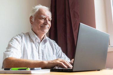 Ana konu odak dışı, kıdemli yaşlı erkek masada oturuyor, ev bilgisayarı çevrimiçi dizüstü bilgisayar iş mesafesi serbest