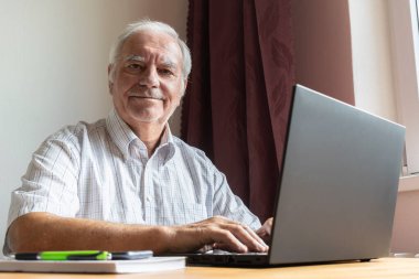 Ana konu odak dışı, kıdemli yaşlı erkek masada oturuyor, ev bilgisayarı çevrimiçi dizüstü bilgisayar iş mesafesi serbest