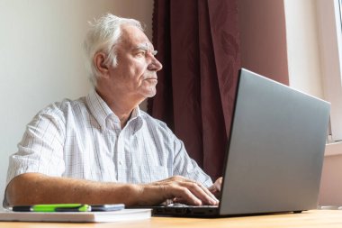 Ana konu odak dışı, kıdemli yaşlı erkek masada oturuyor, ev bilgisayarı çevrimiçi dizüstü bilgisayar iş mesafesi serbest