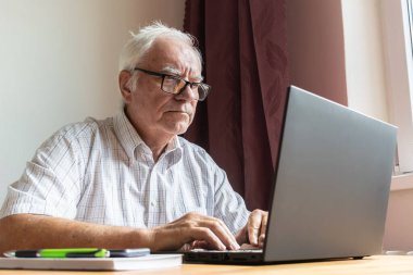 Ana konu odak dışı, kıdemli yaşlı erkek masada oturuyor, ev bilgisayarı çevrimiçi dizüstü bilgisayar iş mesafesi serbest