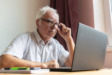 Ana konu odak dışı, kıdemli yaşlı erkek masada oturuyor, ev bilgisayarı çevrimiçi dizüstü bilgisayar iş mesafesi serbest