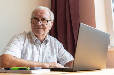 Ana konu odak dışı, kıdemli yaşlı erkek masada oturuyor, ev bilgisayarı çevrimiçi dizüstü bilgisayar iş mesafesi serbest