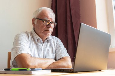 Ana konu odak dışı, kıdemli yaşlı erkek masada oturuyor, ev bilgisayarı çevrimiçi dizüstü bilgisayar iş mesafesi serbest