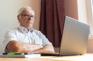 Ana konu odak dışı, kıdemli yaşlı erkek masada oturuyor, ev bilgisayarı çevrimiçi dizüstü bilgisayar iş mesafesi serbest