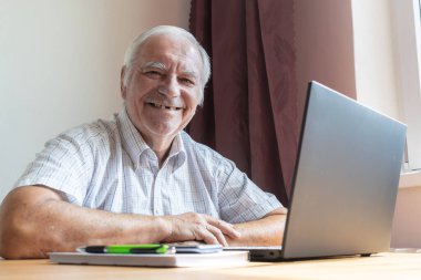 Ana konu odak dışı, kıdemli yaşlı erkek masada oturuyor, ev bilgisayarı çevrimiçi dizüstü bilgisayar iş mesafesi serbest