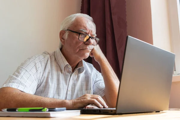 Ana konu odak dışı, kıdemli yaşlı erkek masada oturuyor, ev bilgisayarı çevrimiçi dizüstü bilgisayar iş mesafesi serbest