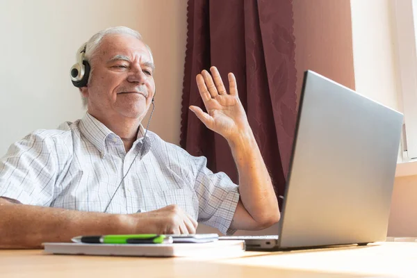 Ana konu odak dışı, kıdemli yaşlı erkek masa başında oturuyor, ev bilgisayarı, dizüstü bilgisayar iş mesafesi serbest müzik kulaklıkları mutlu çağrı merkezleri.