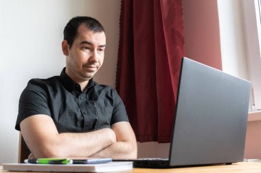 Ana konu odak dışı, genç erkek masa başında oturuyor, ev bilgisayarı çevrimiçi dizüstü bilgisayar çalışıyor iş mesafesi serbest çalışan yorgun