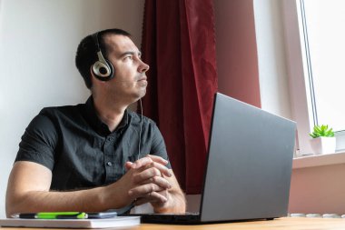 Ana konu odak dışı, genç erkek masa başında oturuyor, ev bilgisayarı online dizüstü bilgisayar iş mesafesi serbest müzik konsantrasyonunu boz