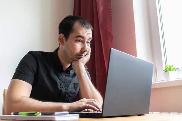 Ana konu odak dışı, genç erkek masa başında oturuyor, ev bilgisayarı çevrimiçi dizüstü bilgisayar çalışıyor iş mesafesi serbest çalışan yorgun