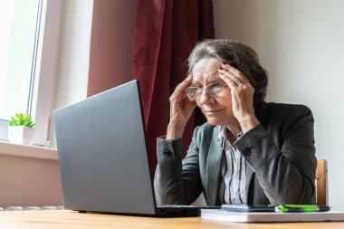 Ana konu odak dışı, yaşlı yaşlı kadın masa başında oturuyor, ev bilgisayarı çevrimiçi dizüstü bilgisayar çalışıyor iş mesafesi serbest çalışan, sıkılmış