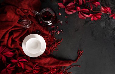 Sonbahar kompozisyonu. Çaydanlıkta Karkade çayı, beyaz fincan ve çay tabağı, bir eşarp ve sonbahar kırmızı üzüm yaprakları. Düz yatıyordu. Üst görünüm.