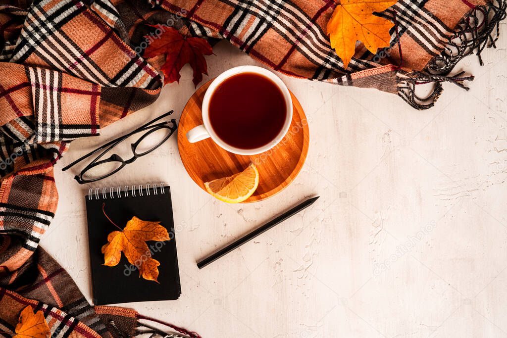 Autumn composition. A cup of tea, scarf, autumn leaves, glasses, notepad, pencil. Flat lay, top view, copy space