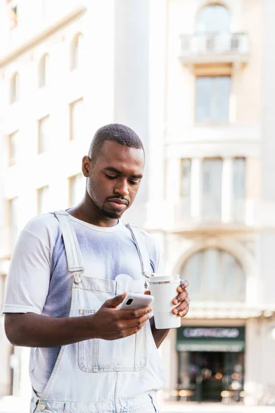 Африканський молодий чоловік ходить по вулицях, дивлячись його телефон — стокове фото