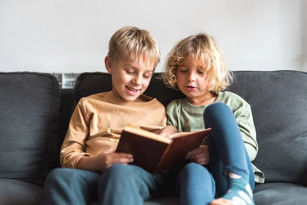 Чарівні маленькі брати і сестри читають книгу на дивані — стокове фото
