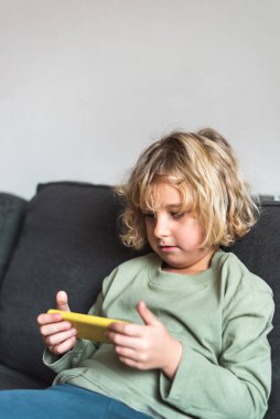 Kanepede akıllı telefondan video oyunu oynayan dikkatli bir çocuk.