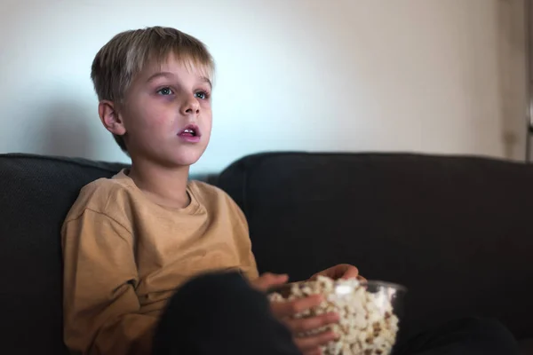 Kanepede TV izlerken patlamış mısır yiyen meraklı çocuk.