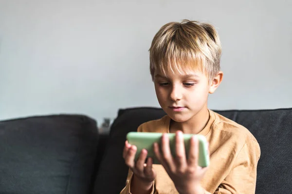 Kid using smartphone sitting on sofa at home