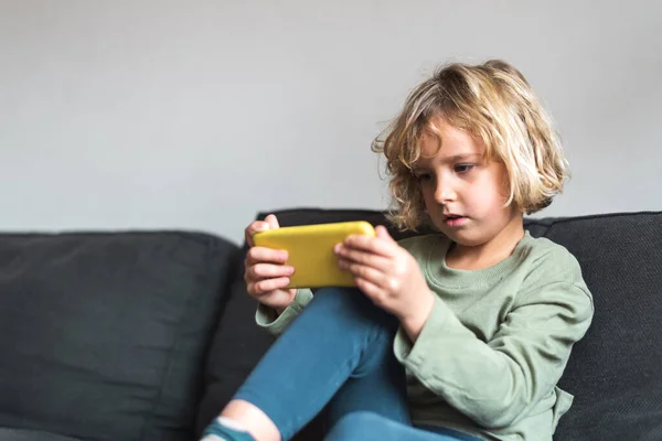 Niño concentrado jugando videojuego en el teléfono inteligente en casa —  Fotos de Stock