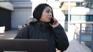 Bilgisayarla çalışırken akıllı telefondan konuşan etnik bir kadın.