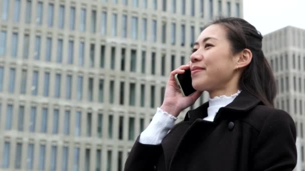 Chinese entrepreneur speaking on mobile phone near skyscrapers — Stock Video