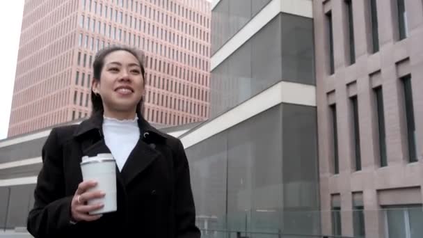 Happy Asian businesswoman with takeaway coffee walking in downtown — Stock Video