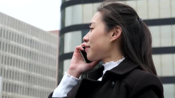 Kinesisk affärskvinna talar på mobiltelefon mot skyskrapor — Stockvideo