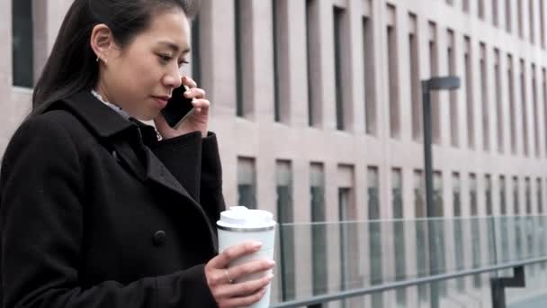 Asiatisk affärskvinna med hämtmat kaffe talar på smartphone — Stockvideo