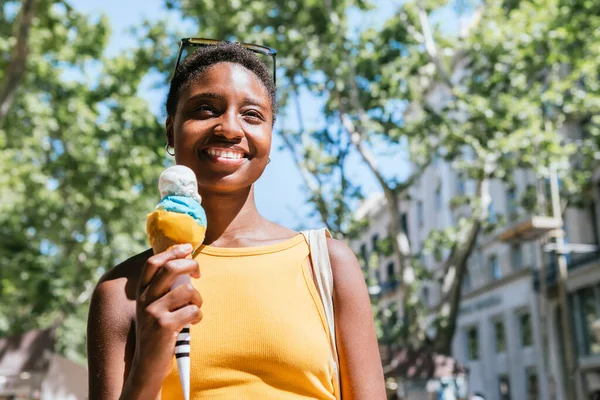 smiling african woman walking the street with a cone ice-cream on her hand