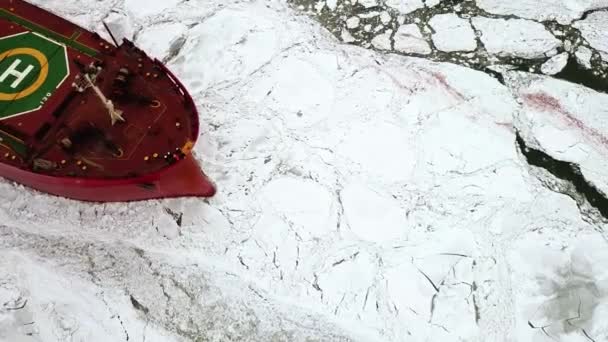 Drone haut vers le bas Epic brise-glace en acier rouge navire citerne brise la mer gelée d'hiver, surmonte. La proue du navire flotte à travers la banquise. Énorme bloc blanc de glace. — Video
