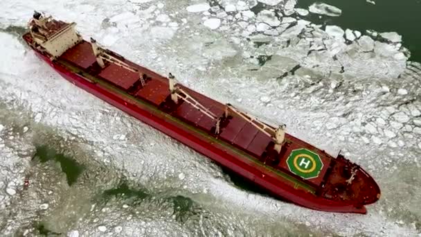 Aérea por encima de la épica gran rompehielos de acero rompe el hielo por el arco del barco y flota en grandes témpanos de hielo marino. Mantener la navegación en un canal de mar congelado. Buque autopropulsado especializado buque rojo — Vídeo de stock