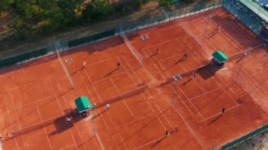 Tenis oyuncuları profesyonel stadyumda maç sırasında hareket halindeler. Hava görüntüsü. Oyuncular turuncu sahada tenis oynuyorlar.